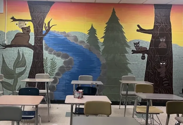A classroom wall painted with a sunset forest, a winding river, tall pines and owl and raccoon friends in the trees
